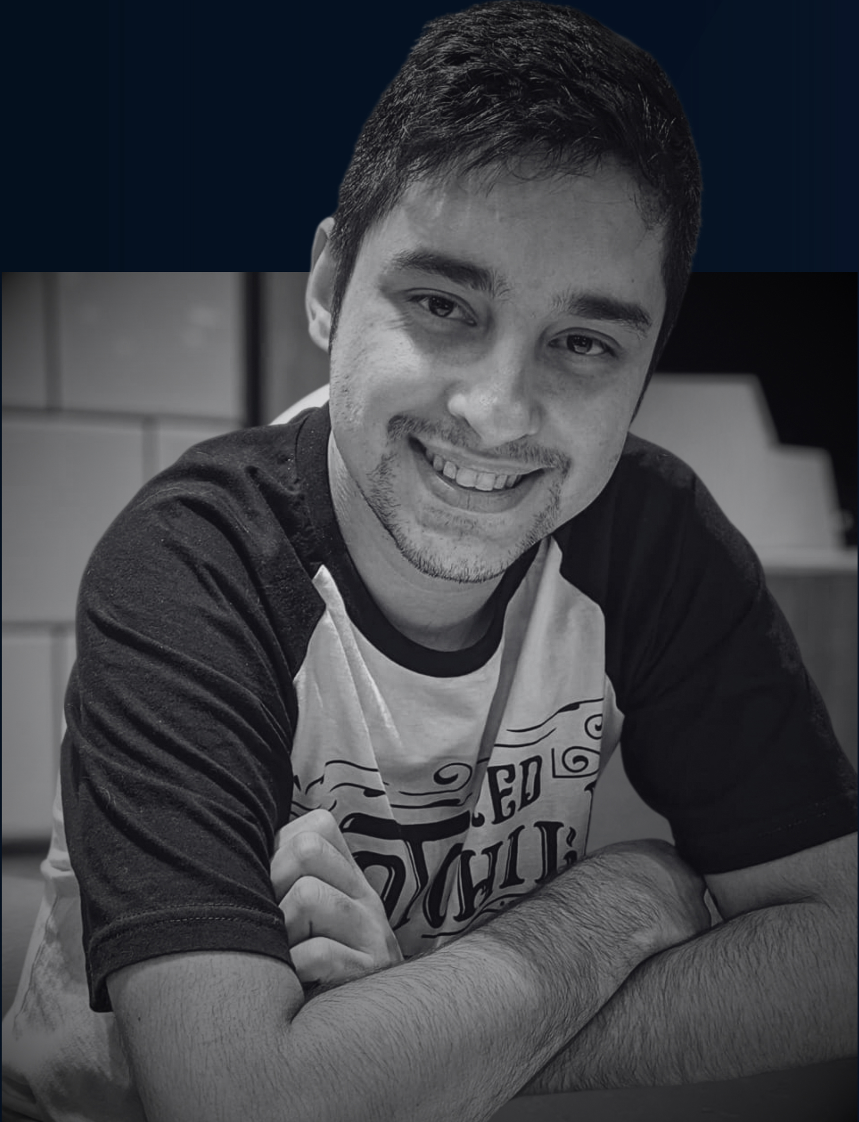 foto preto e branco de homem sentado em uma mesa com os braços cruzados enquanto sorri para a foto